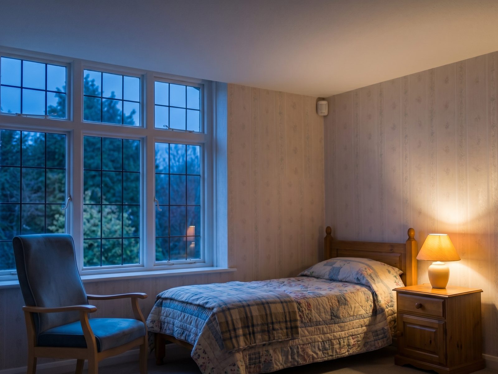 The same style of room at night, softly lit, with the wall-mounted sensor keeping watch